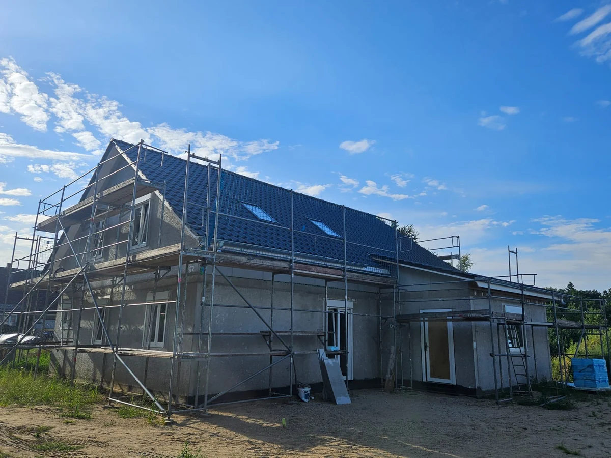 Scaffolded house with a finished dark tiled roof, windows and doors installed