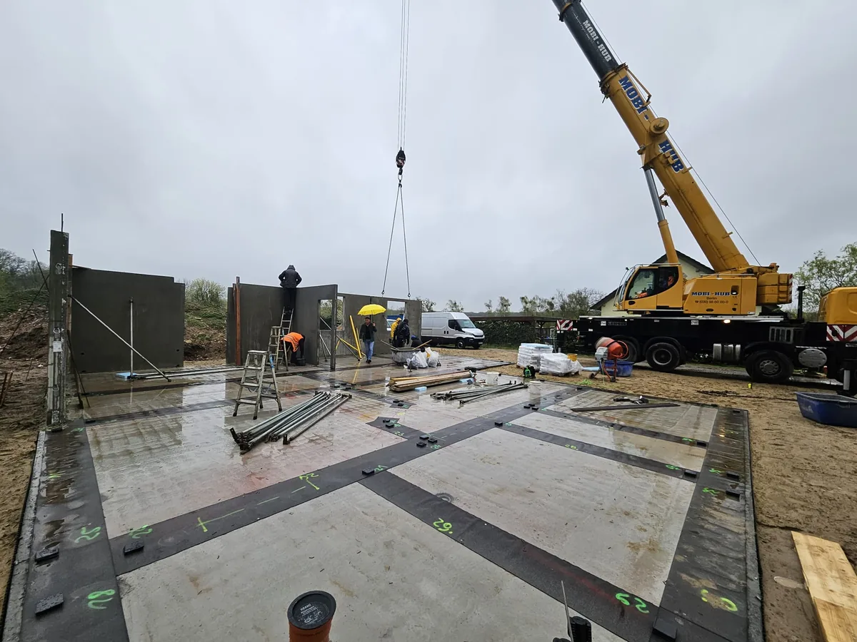 A mobile crane sets precast concrete wall elements onto the floor slab